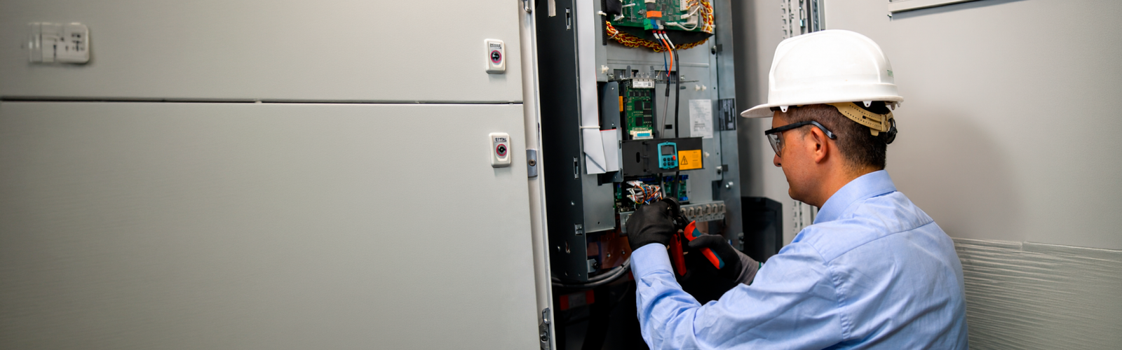 Técnico industrial realizando revisión de componentes eléctricos dentro de un tablero de control en entorno de planta.